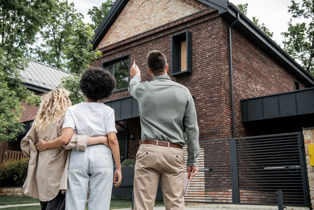 back view of a real estate broker showing a new cottage to an interracial, lesbian couple outdoors