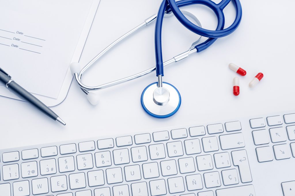Doctor desk with Stethoscope, computer keyboard and medicine pills on white background. Health care or pharmacy concept background. Top view