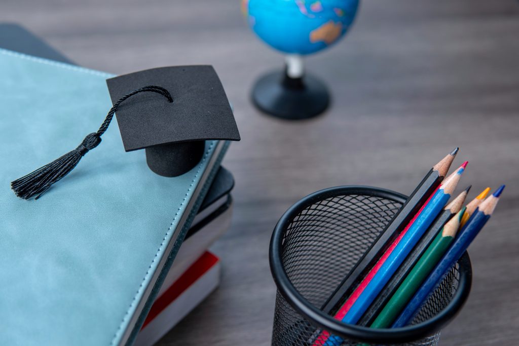 Graduation cap on top of a stack of books, a globe, and a collection of colored pencils. Education and learning concept.