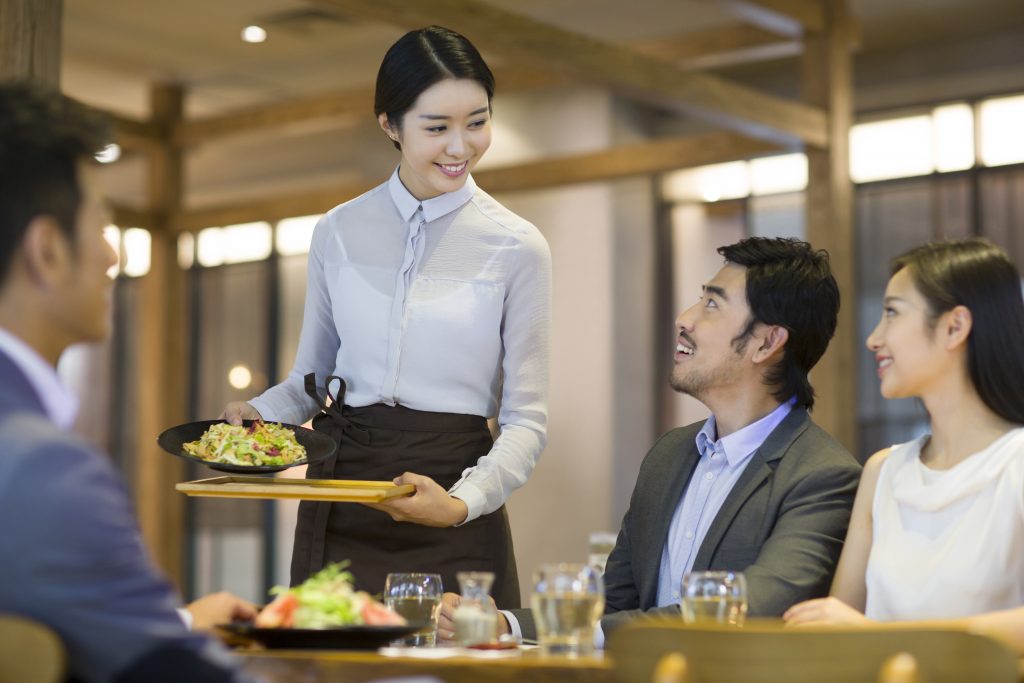 An Asian waitress serves a table of people their food, they are dressed in casual business attire for a meeting in the restaurant