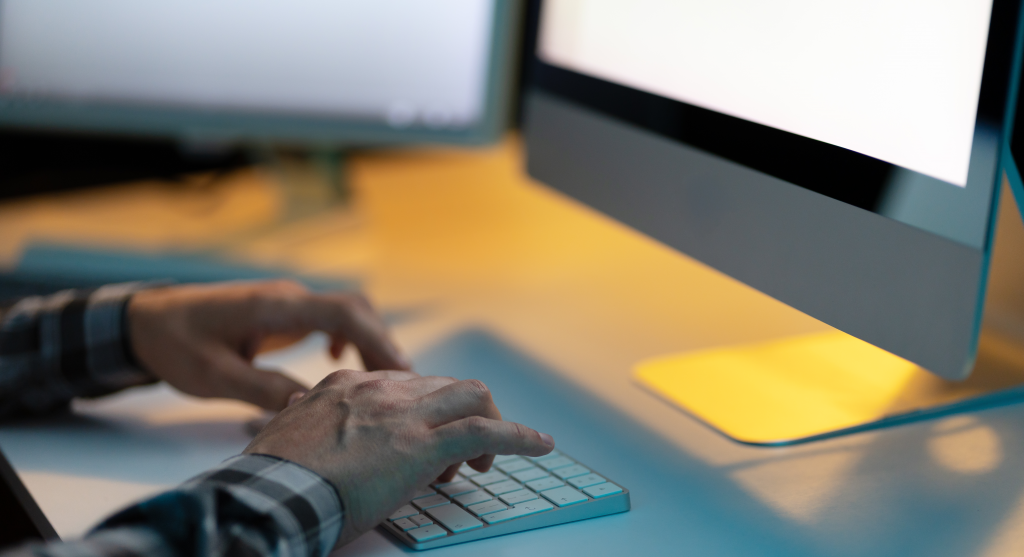 Person Typing On Keyboard In Low Light Workspace, Desktop Computer, Evening Work Environment, Focused, Technology, Office Setting, Cozy Ambiance, Productivity