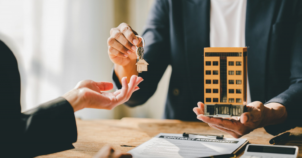 a real estate agent holding a small model of a building while handing over the keys to a client